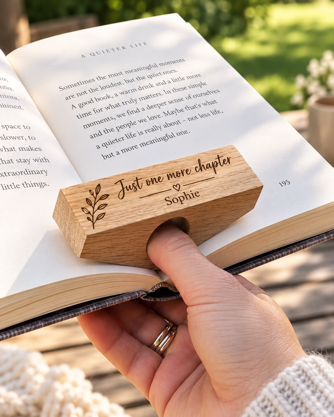 Personalised oak book page holder engraved with “Just one more chapter” and “Sophie”, used to hold an open book with one hand.