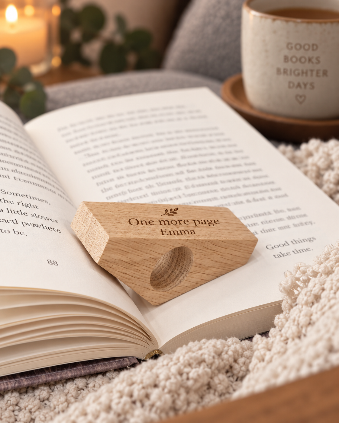 Personalised oak book page holder engraved with “One more page” and “Emma”, resting on an open book in a warm reading setting.